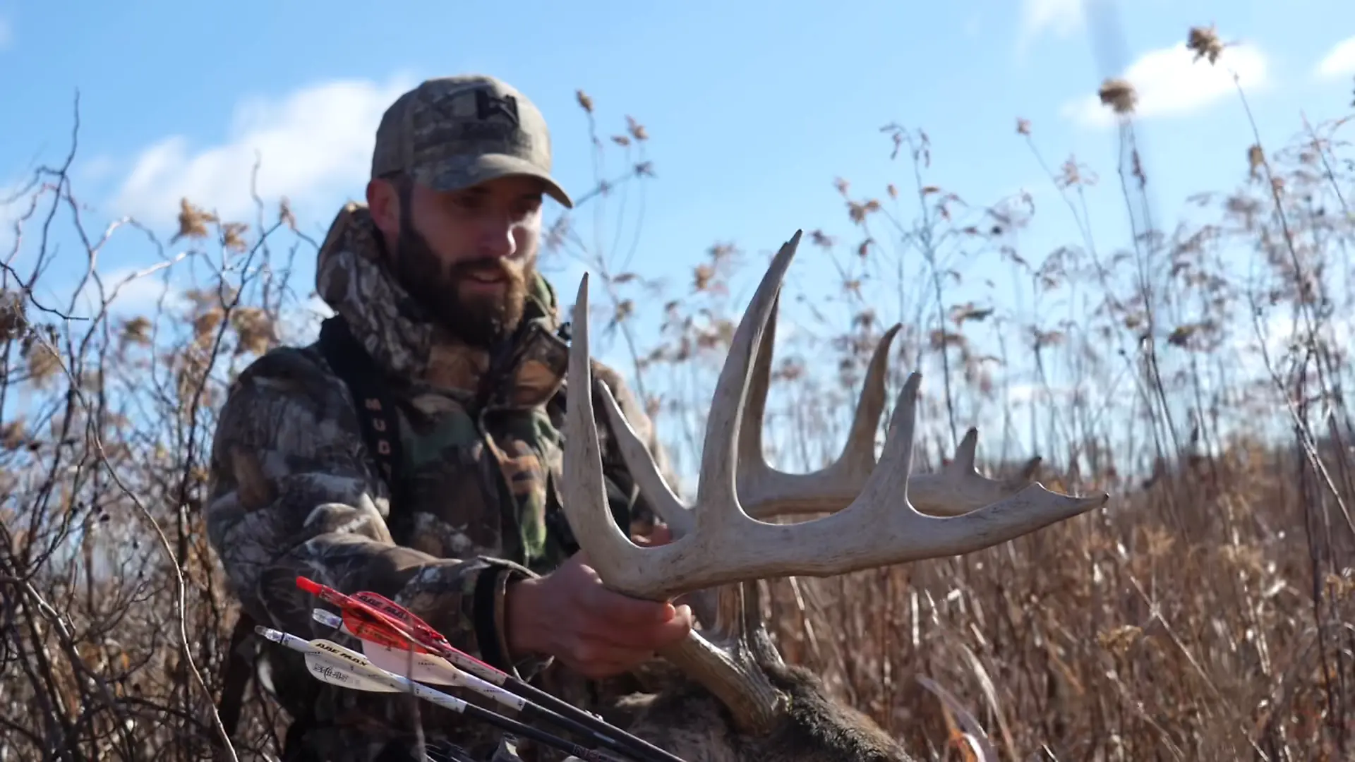Kaleb Greiner kneeling in a field holding a mature Iowa whitetail buck